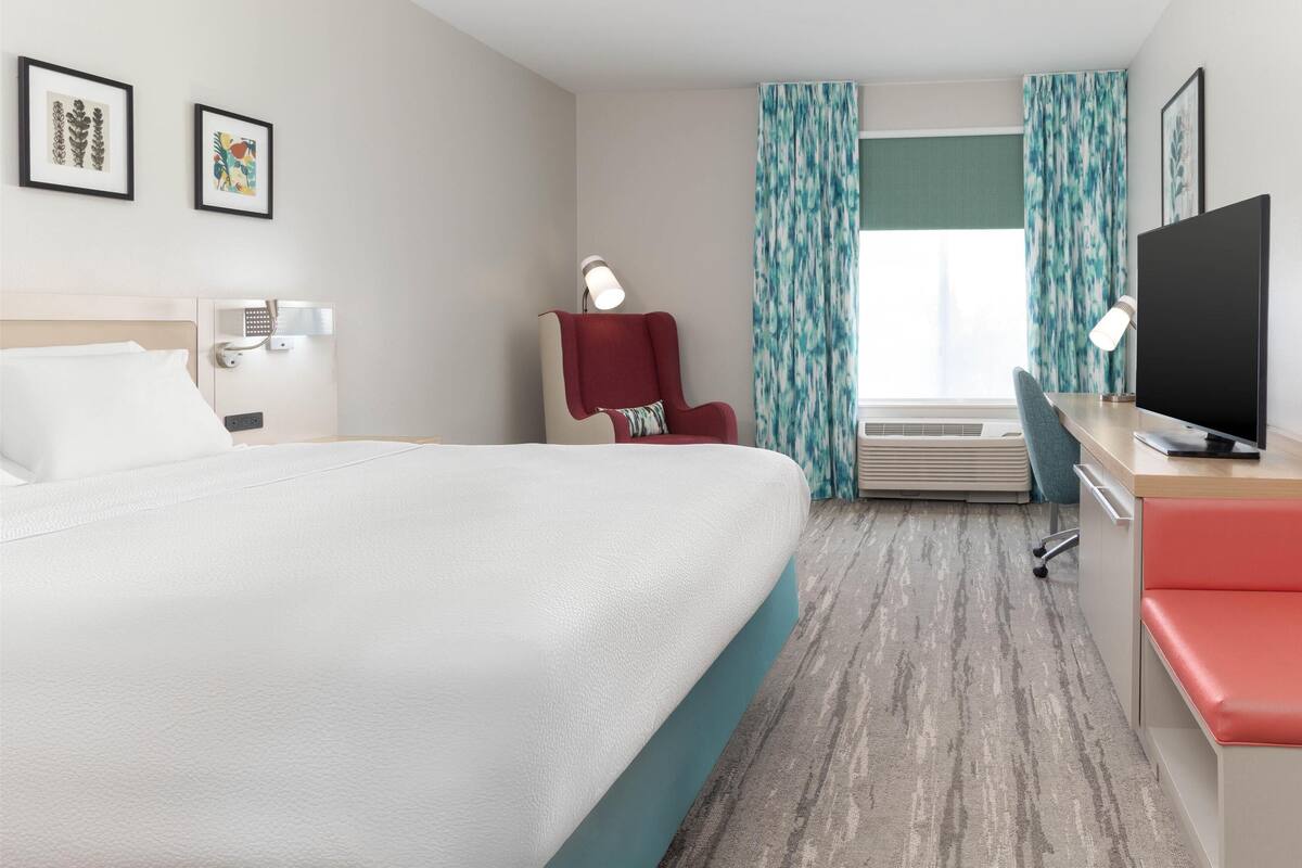 Een hotelkamer met een groot bed, een bureau met een computer, een stoel en een televisie.