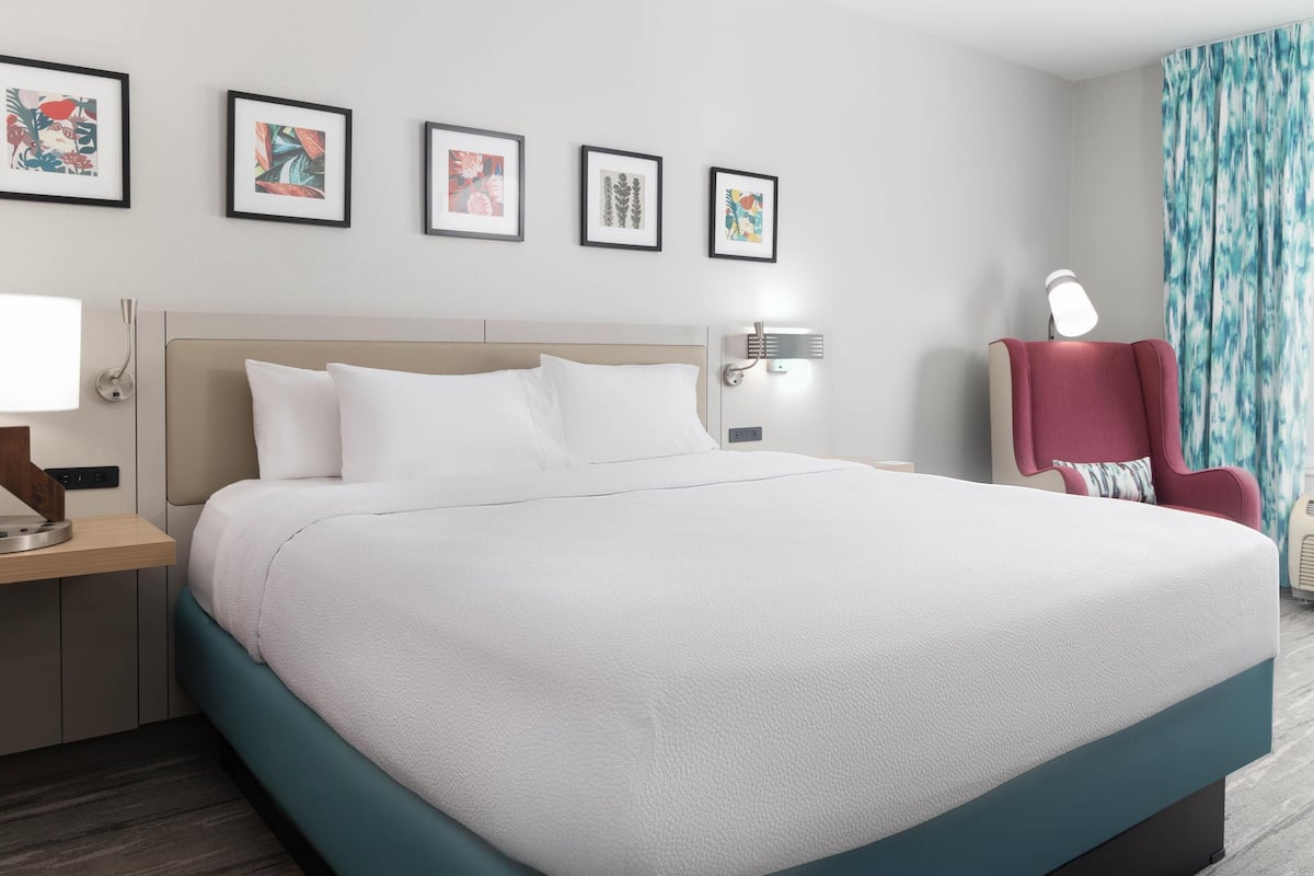 Een net opgemaakt bed met witte lakens, een hoofdbord en een nachtkastje met een lamp.