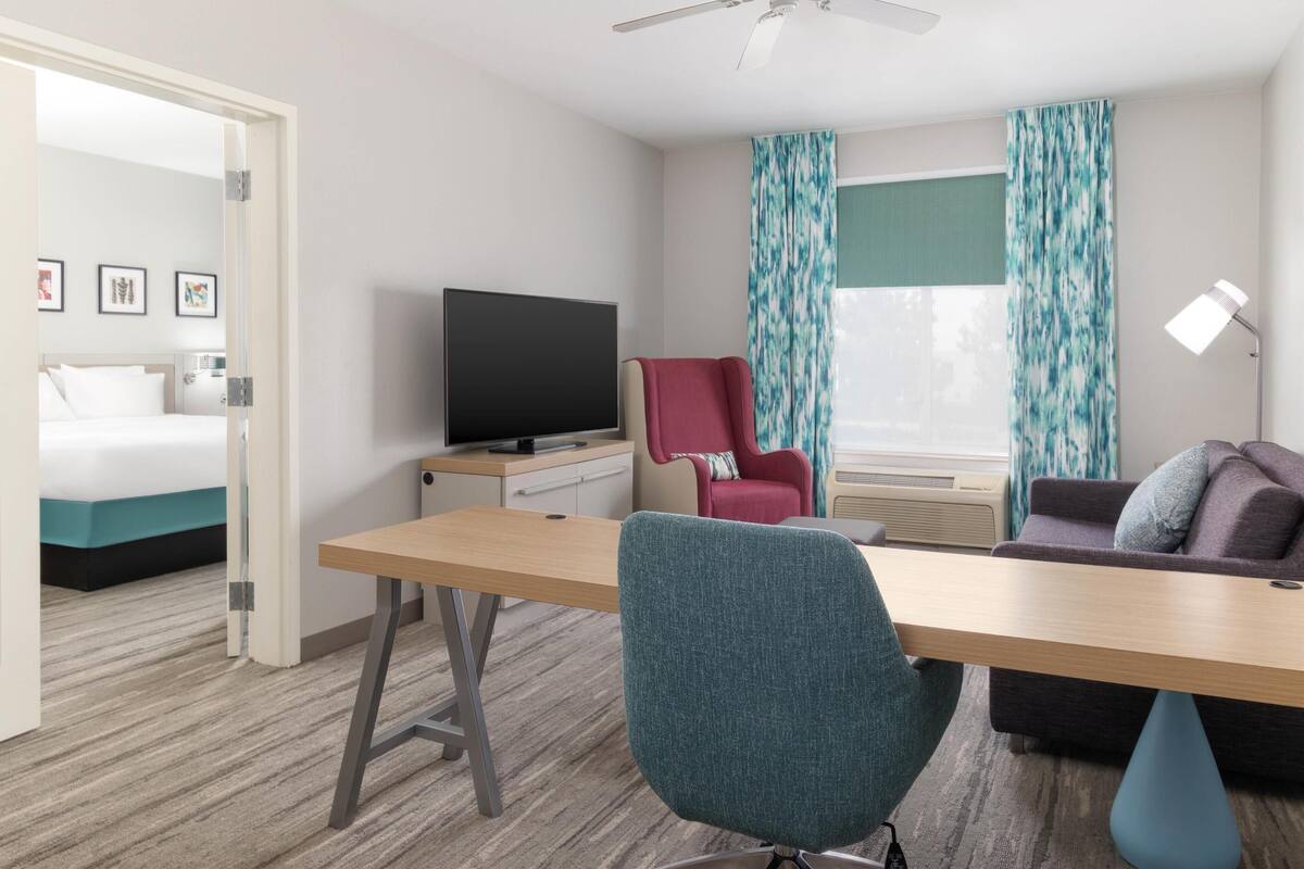 Een hotelkamer met een bed, een bureau, een televisie, een rode stoel, een bank en een raam met gordijnen.