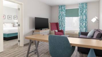 Een hotelkamer met een bed, een bureau, een televisie, een rode stoel, een bank en een raam met gordijnen.