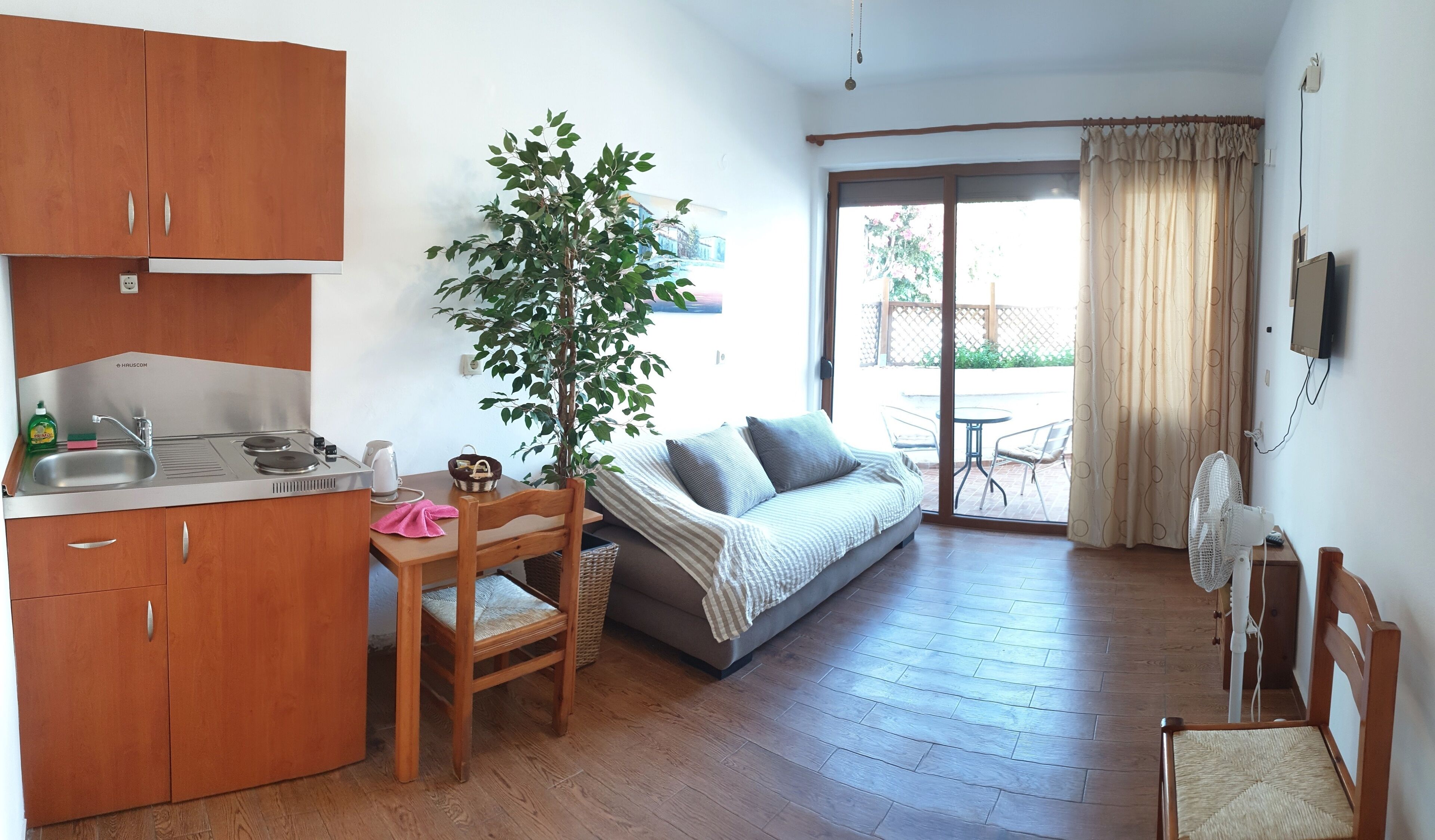 A compact living space with a kitchenette, a dining area, a sofa, and a sliding glass door leading to an outdoor patio.