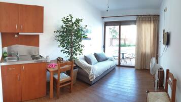 A compact living space with a kitchenette, a dining area, a sofa, and a sliding glass door leading to an outdoor patio.