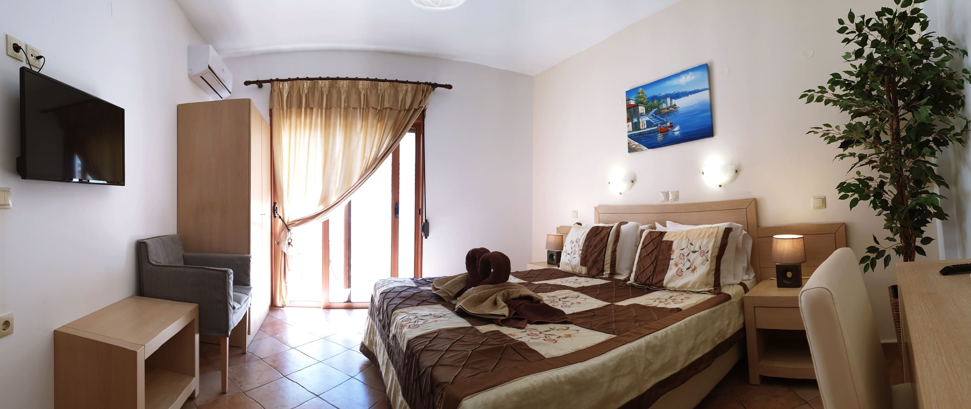 Habitación de hotel con cama, escritorio, silla, televisor, un cuadro y una planta en maceta.