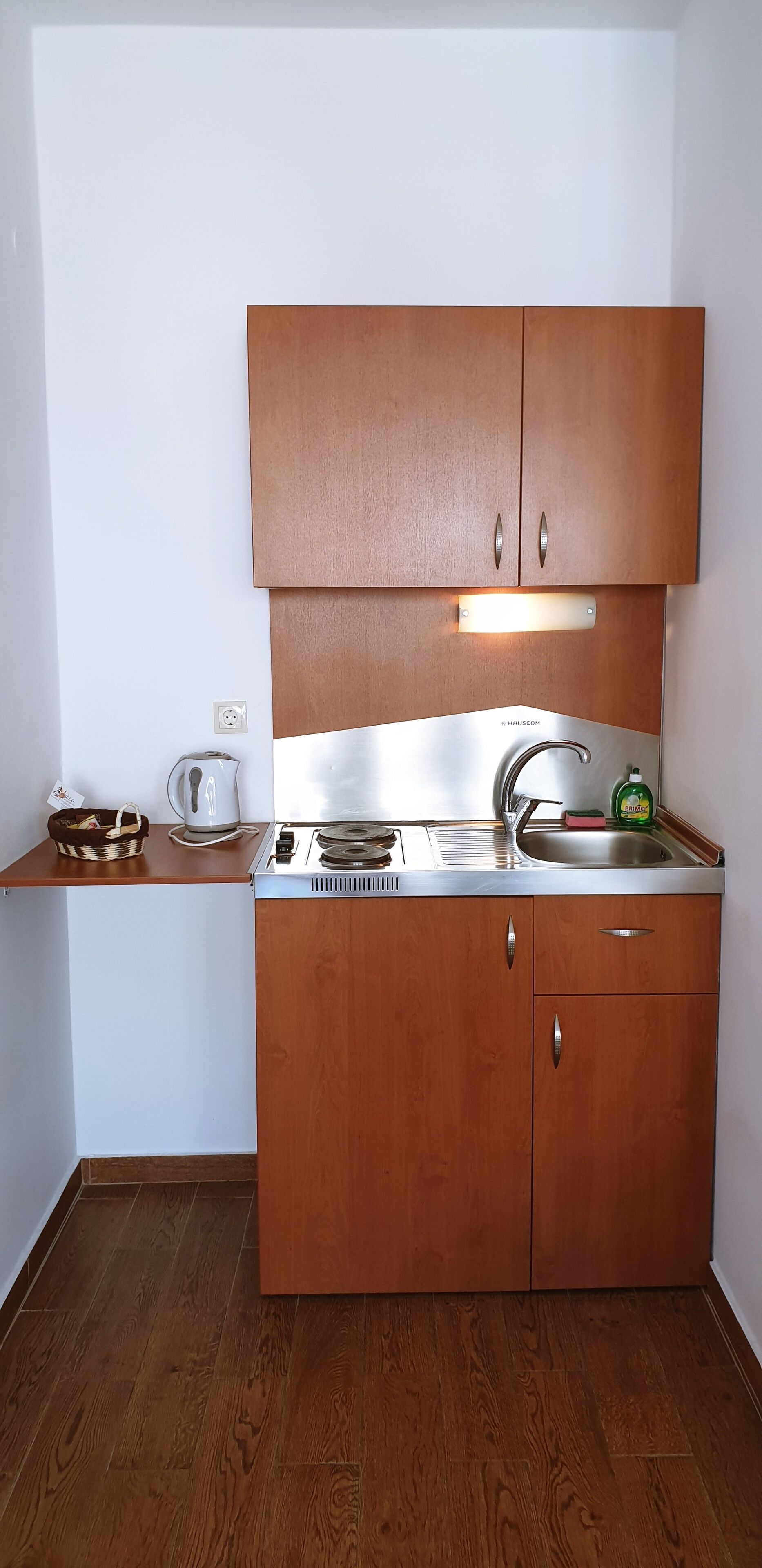 Una cocina compacta con armarios de madera, estufa integrada, un fregadero y una tetera.