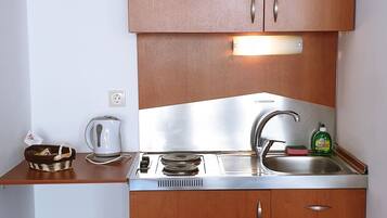 Una cocina compacta con armarios de madera, estufa integrada, un fregadero y una tetera.