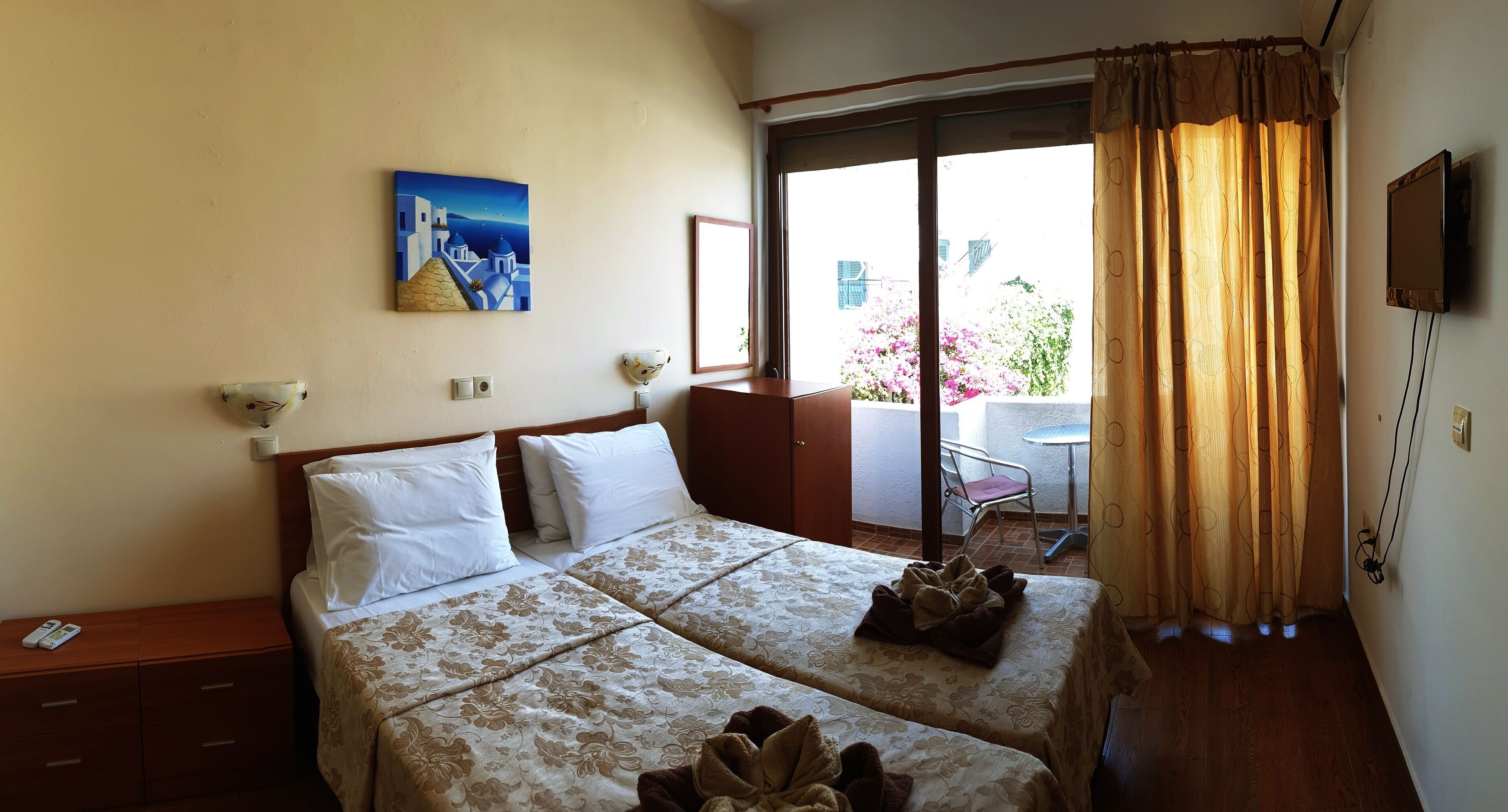 Quarto de hotel com duas camas, um quadro, televisão e varanda florida.