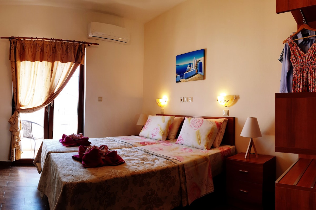 A hotel room with a bed, a nightstand, a lamp, a painting, and a window with curtains.