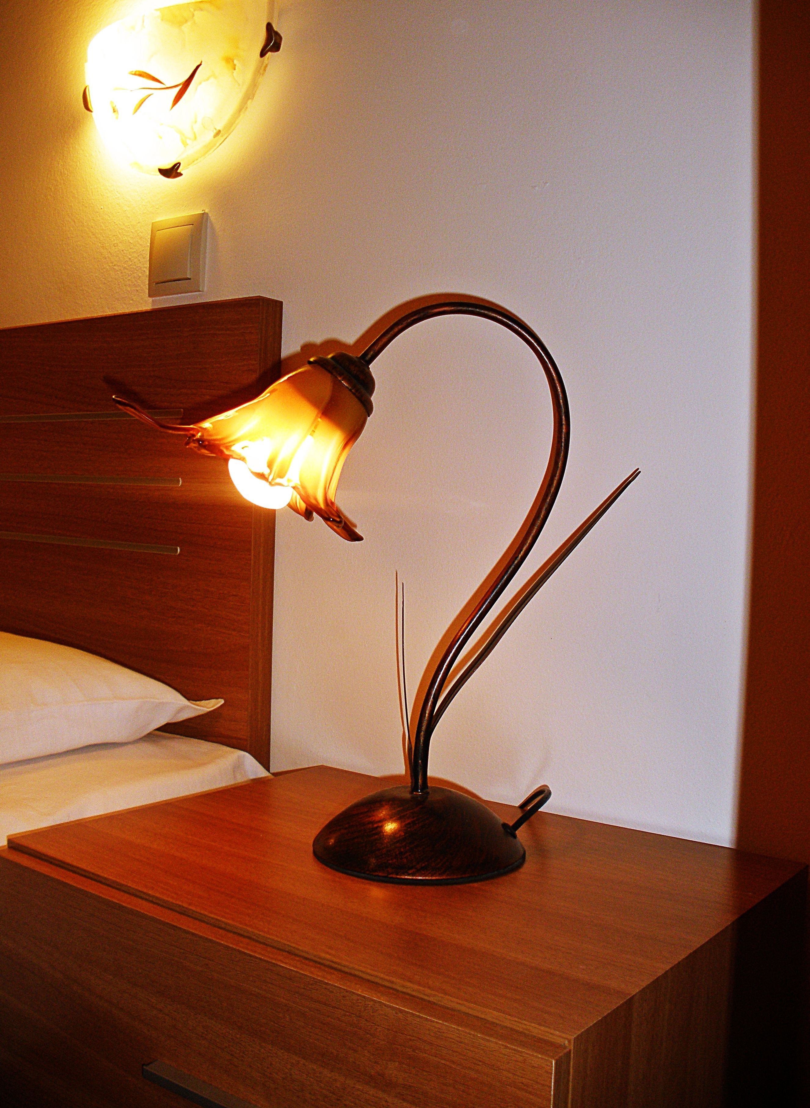A bedside table with a unique lamp, a wooden headboard, and a wall clock.
