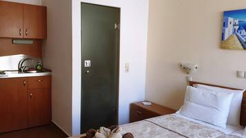 A hotel room with a bed, a nightstand, a painting, and a kitchenette with a sink and cabinets.