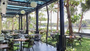 An outdoor dining area with tables and chairs, surrounded by greenery and a view of a body of water. - Indochine Hoi An Hotel (Hoi An)