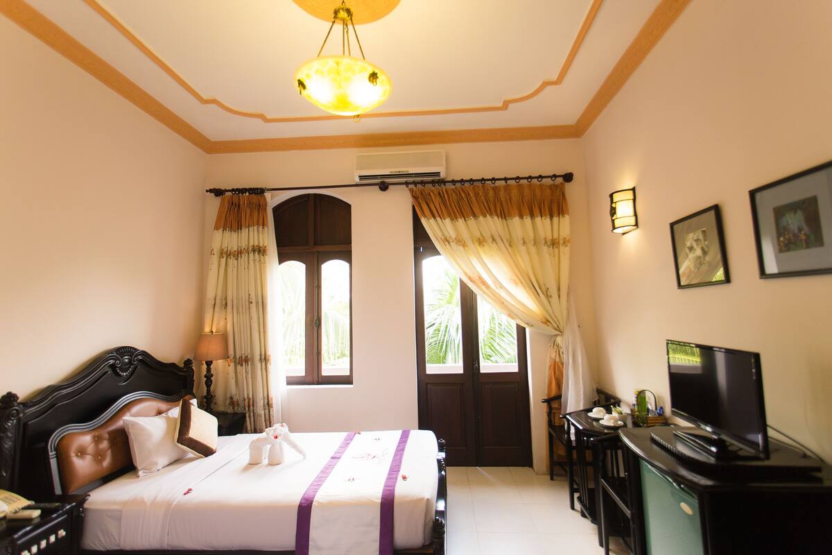 A hotel room with a bed, a desk with a computer, a television, and a window with curtains.