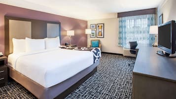 A hotel room with a large bed, a desk with a television, and a window with patterned curtains.