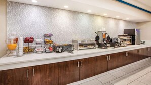 A breakfast bar with various food items, a coffee machine, and a fruit display.