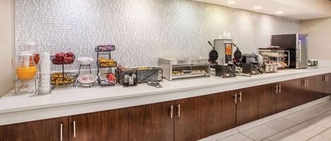 A breakfast bar with various food items, a coffee machine, and a fruit display.