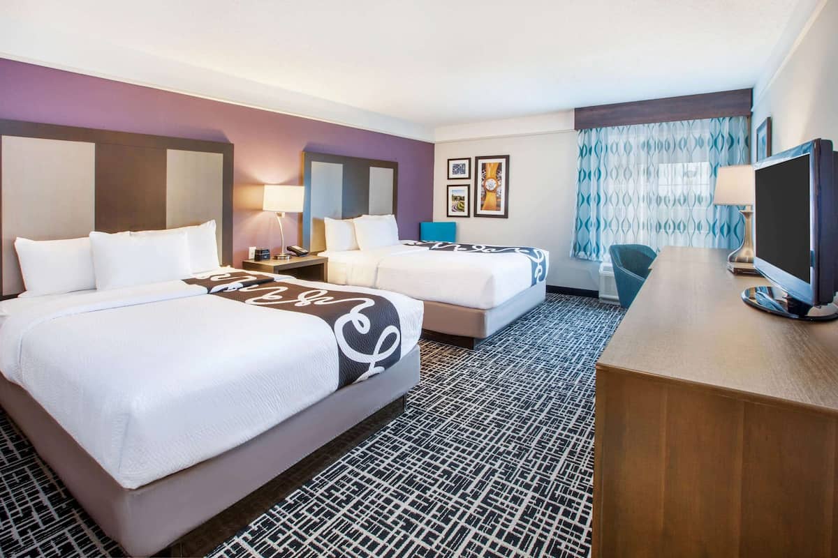 A hotel room with two beds, a desk, a television, and a patterned carpet.