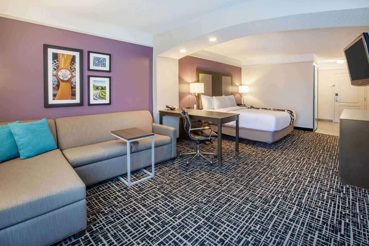 A hotel room with a sofa, a desk, a bed, and a TV.