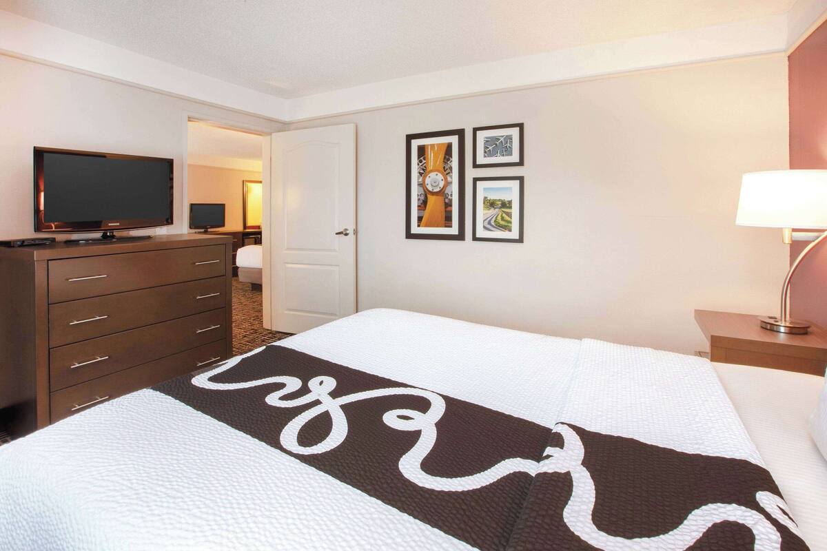 A hotel room with a bed, a TV, a dresser, and framed pictures on the wall.