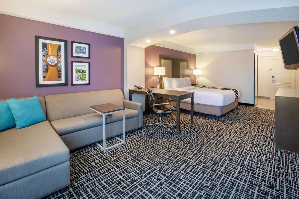 A hotel room with a sofa, a desk, a bed, and a TV.