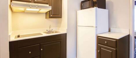 A compact kitchen with dark cabinets, a white countertop, a built-in microwave, and a refrigerator.
