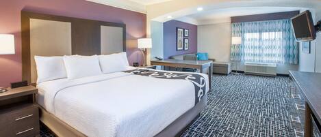A hotel room with a large bed, a desk, a chair, and a television.