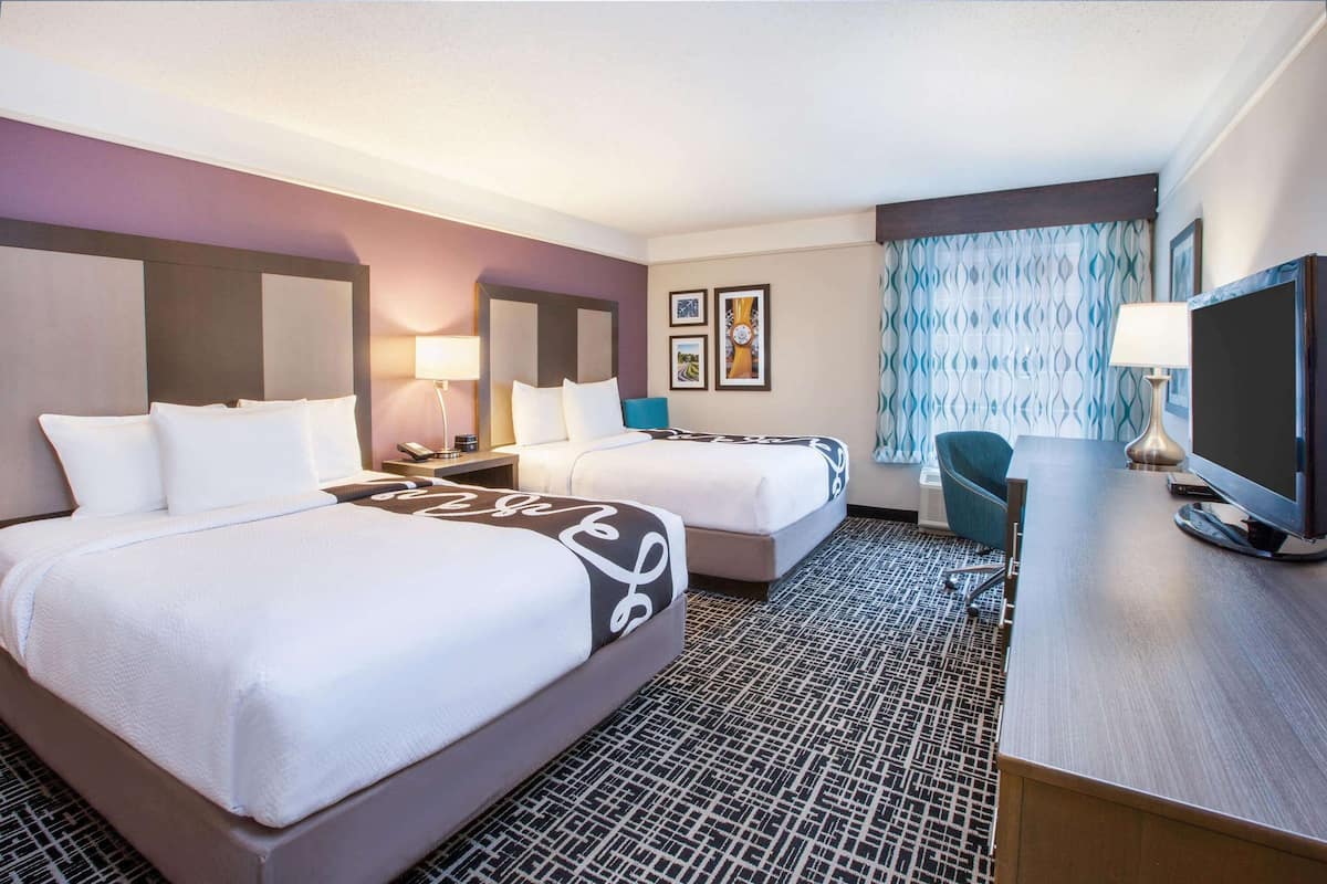 A hotel room with two beds, a desk, a TV, and a chair.