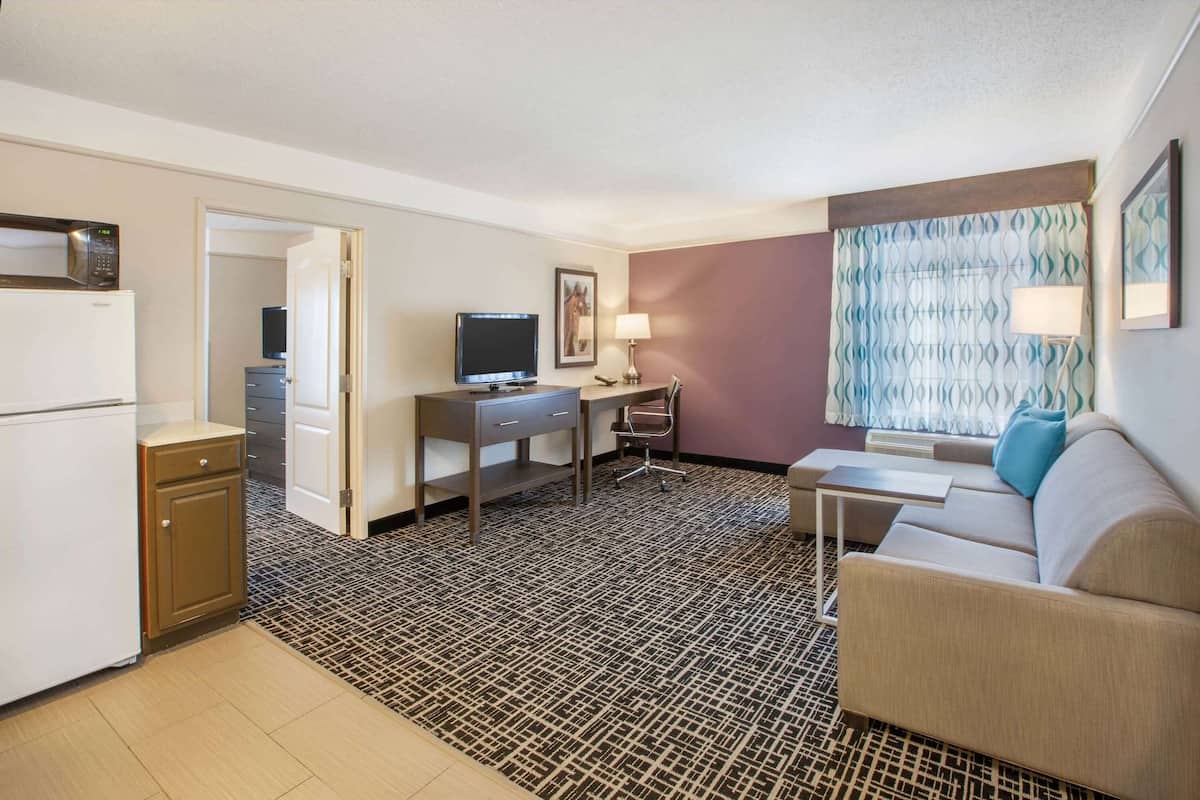 A hotel room with a kitchenette, a desk with a computer, a sofa, and a patterned carpet.