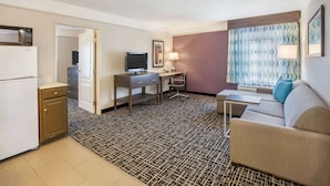 A hotel room with a kitchenette, a desk with a computer, a sofa, and a patterned carpet.
