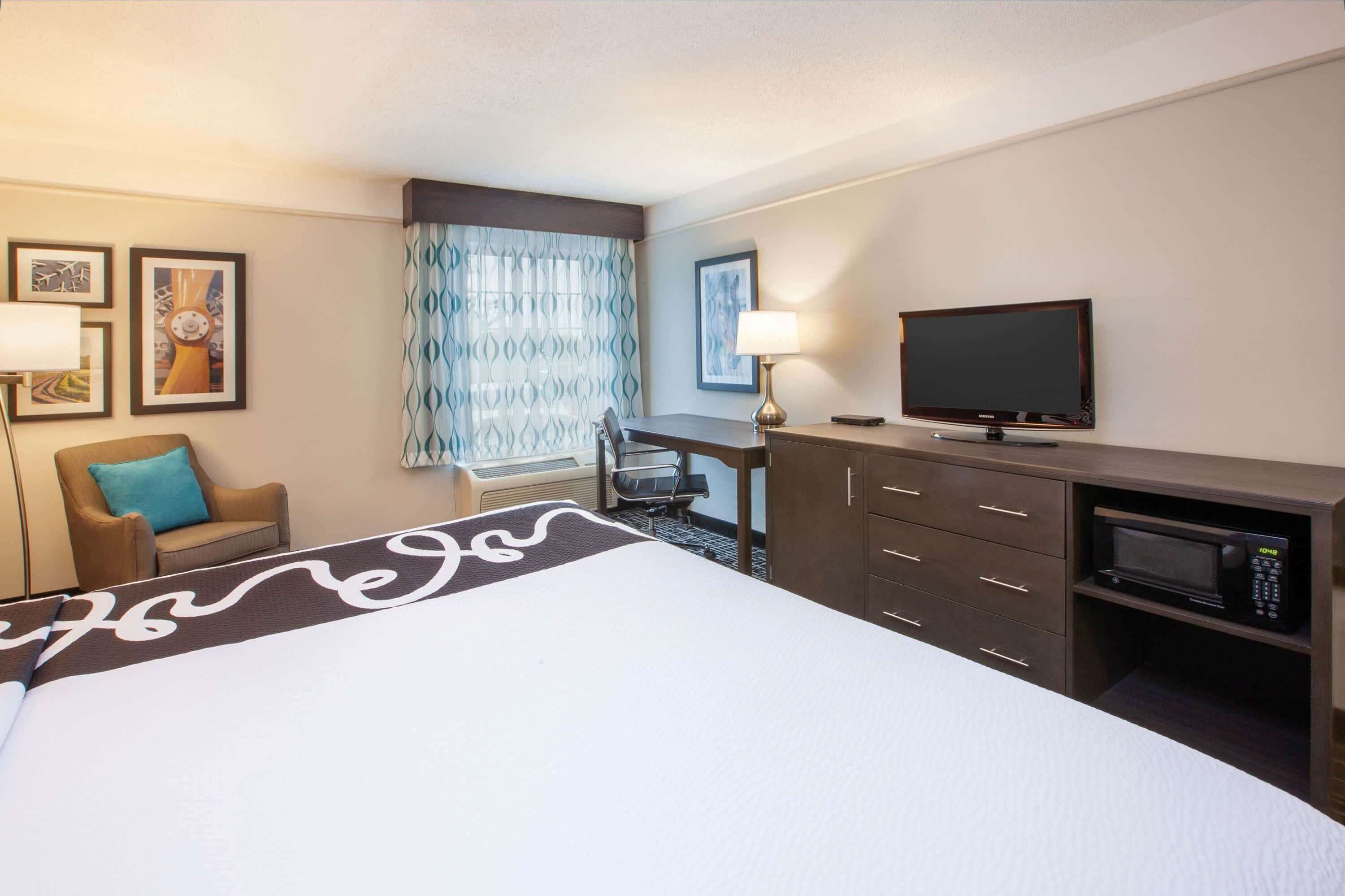 A hotel room with a bed, a desk with a chair, a television, a microwave, and a window with curtains.