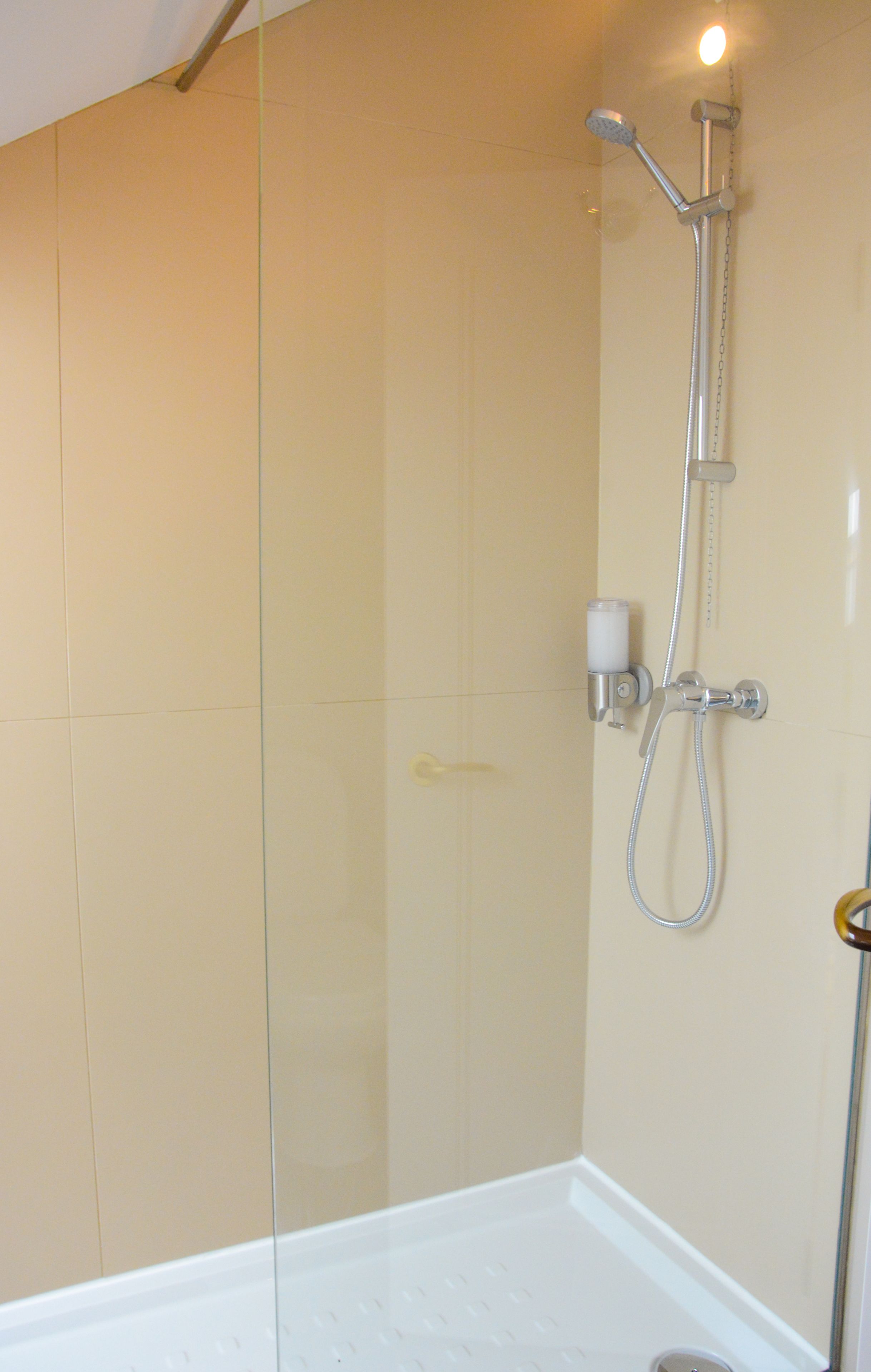 Una ducha con cabezal de ducha de mano y grifo empotrado en la pared, dispensador de jabón y un pequeño recipiente.