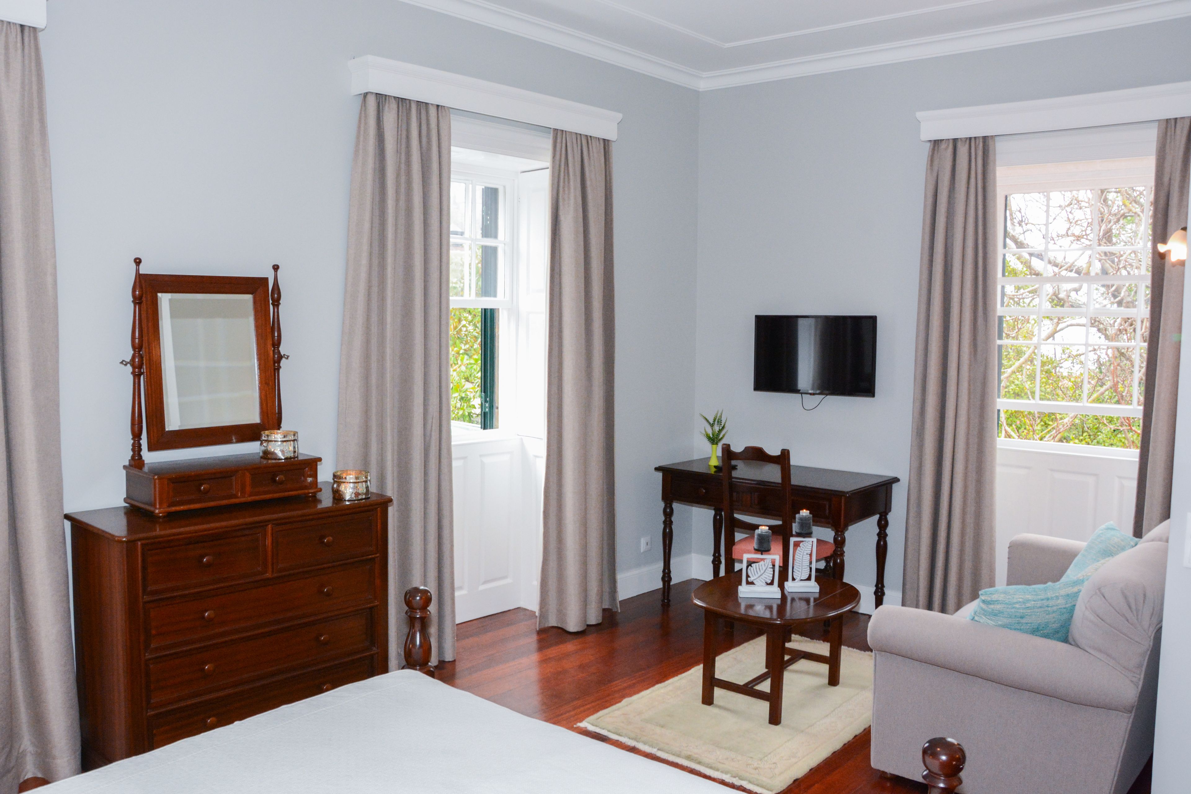 A room with a wooden dresser, a television mounted on the wall, a sofa, and a chair.