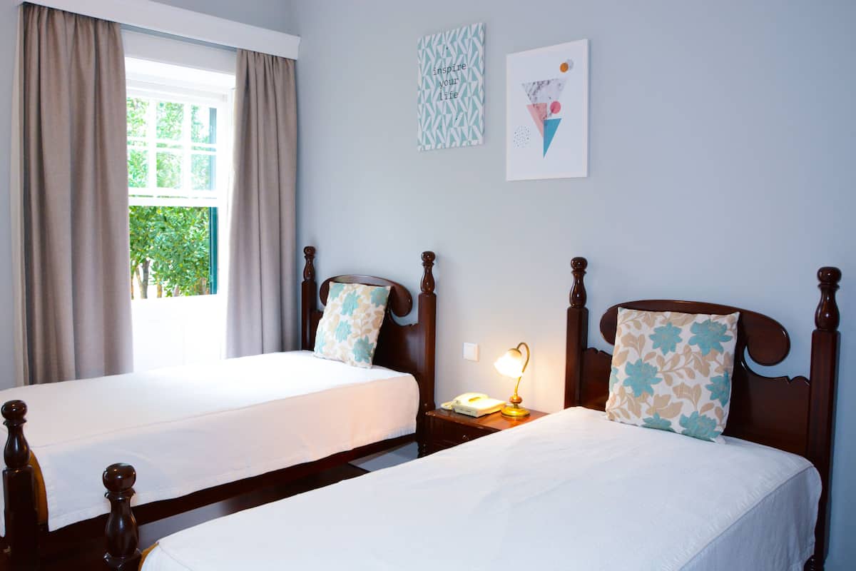 Habitación de hotel con dos camas, una ventana con cortinas, una lámpara de noche y decoración en la pared.