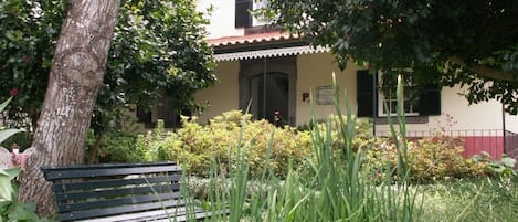 A building with a garden area, a bench, and a tree.