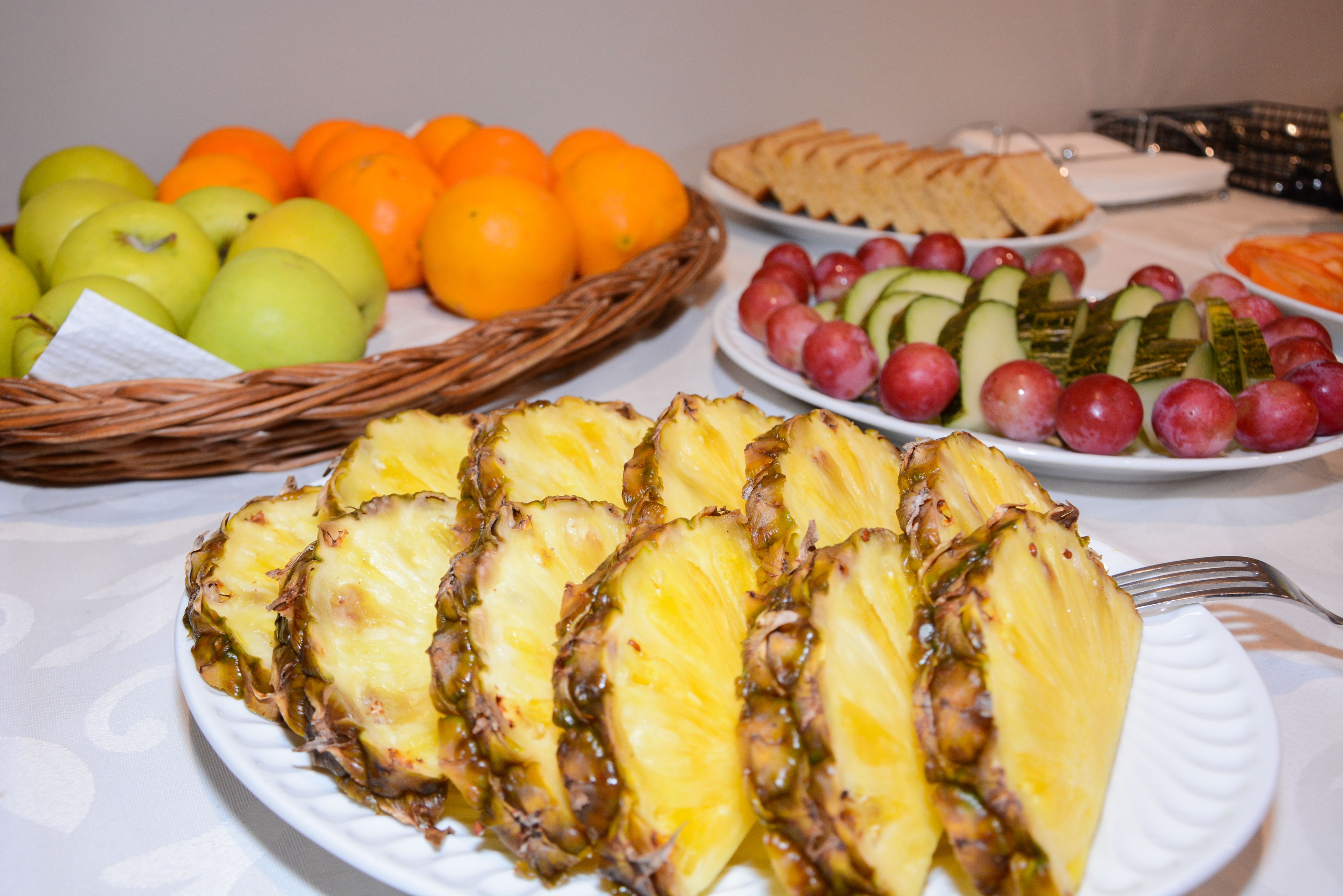 A table with various fruits and snacks, including sliced pineapple, apples, oranges, grapes, and cucumber slices.