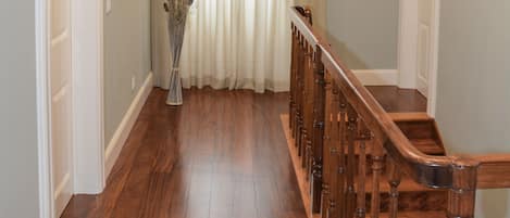 Un pasillo con suelo de madera, una escalera de madera y una lámpara colgante.