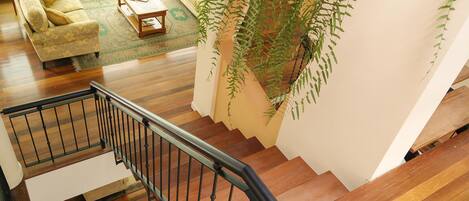 A staircase with wooden steps and a black railing leading to a living room with a sofa, a coffee table, and a large green plant.