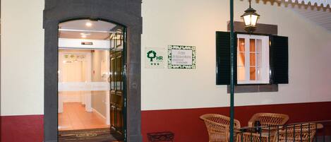 A hotel entrance with a glass door, a sign indicating solar energy use, wicker furniture outside, and a tiled roof.