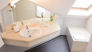 A modern bathroom with a large mirror, two sinks, a bathtub, and a skylight.
