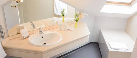 A modern bathroom with a large mirror, two sinks, a bathtub, and a skylight.