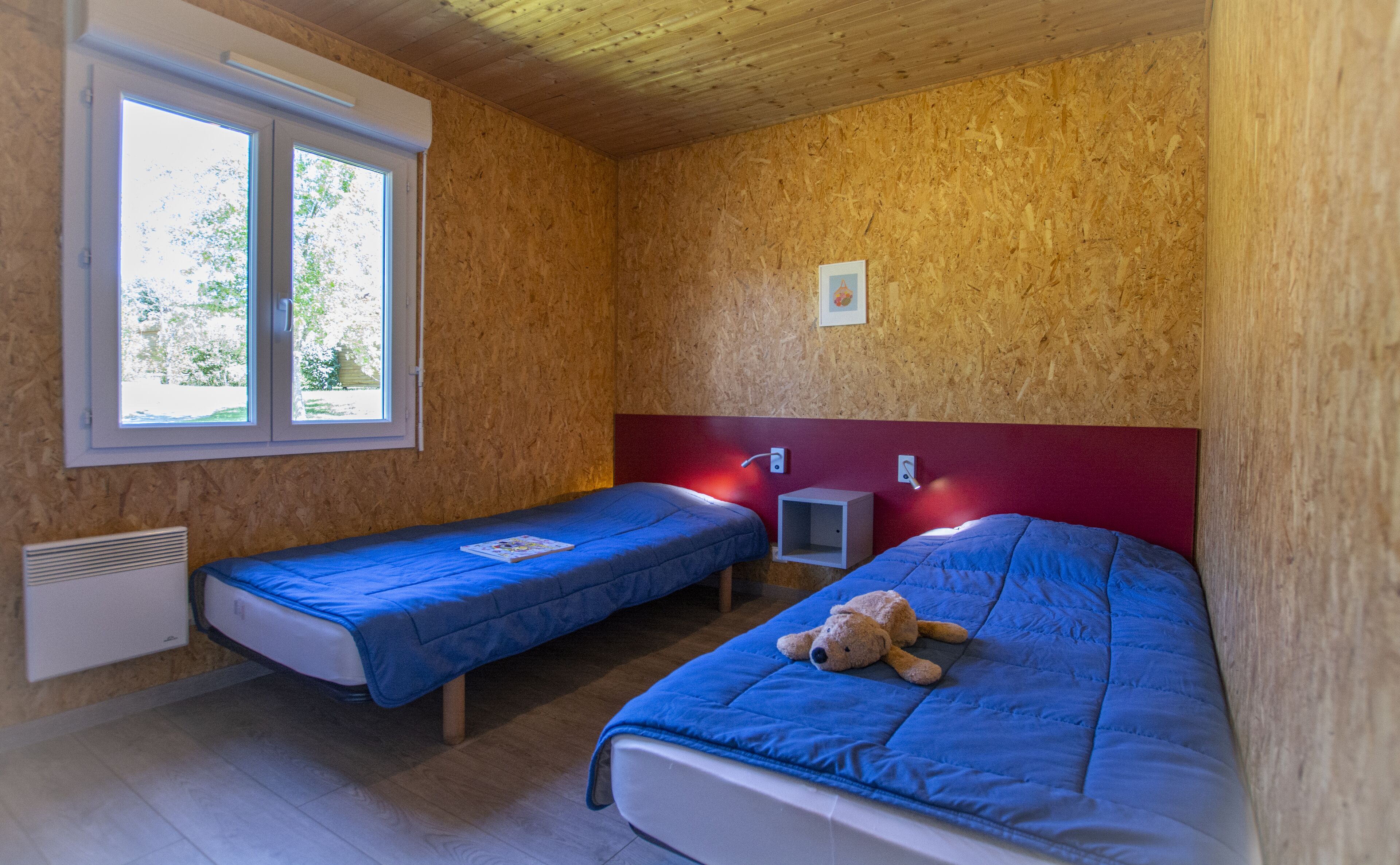 A room with two single beds, a window, and a red headboard.