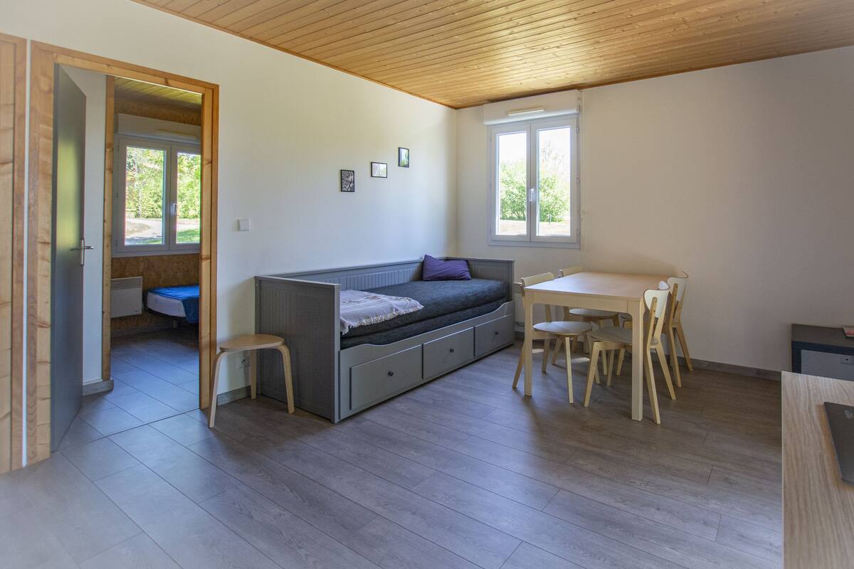 Une pièce compacte comprenant un canapé intégré, une petite table à manger avec des chaises et une fenêtre laissant entrer la lumière naturelle.