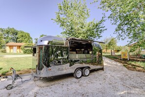 Une camionnette-restaurant est stationnée sur un chemin de gravier, avec des arbres et un bâtiment en arrière-plan.