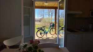 An open door leading to a balcony with bicycles, a white table with flowers, and a kitchen area. - Domaine de la Vingeanne (Villegusien-le-Lac)