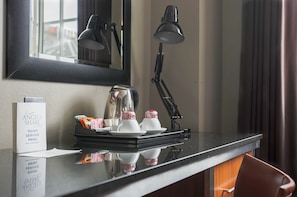 Un bureau dans une chambre d’hôtel, avec une machine à café, une lampe et un présentoir à menus.