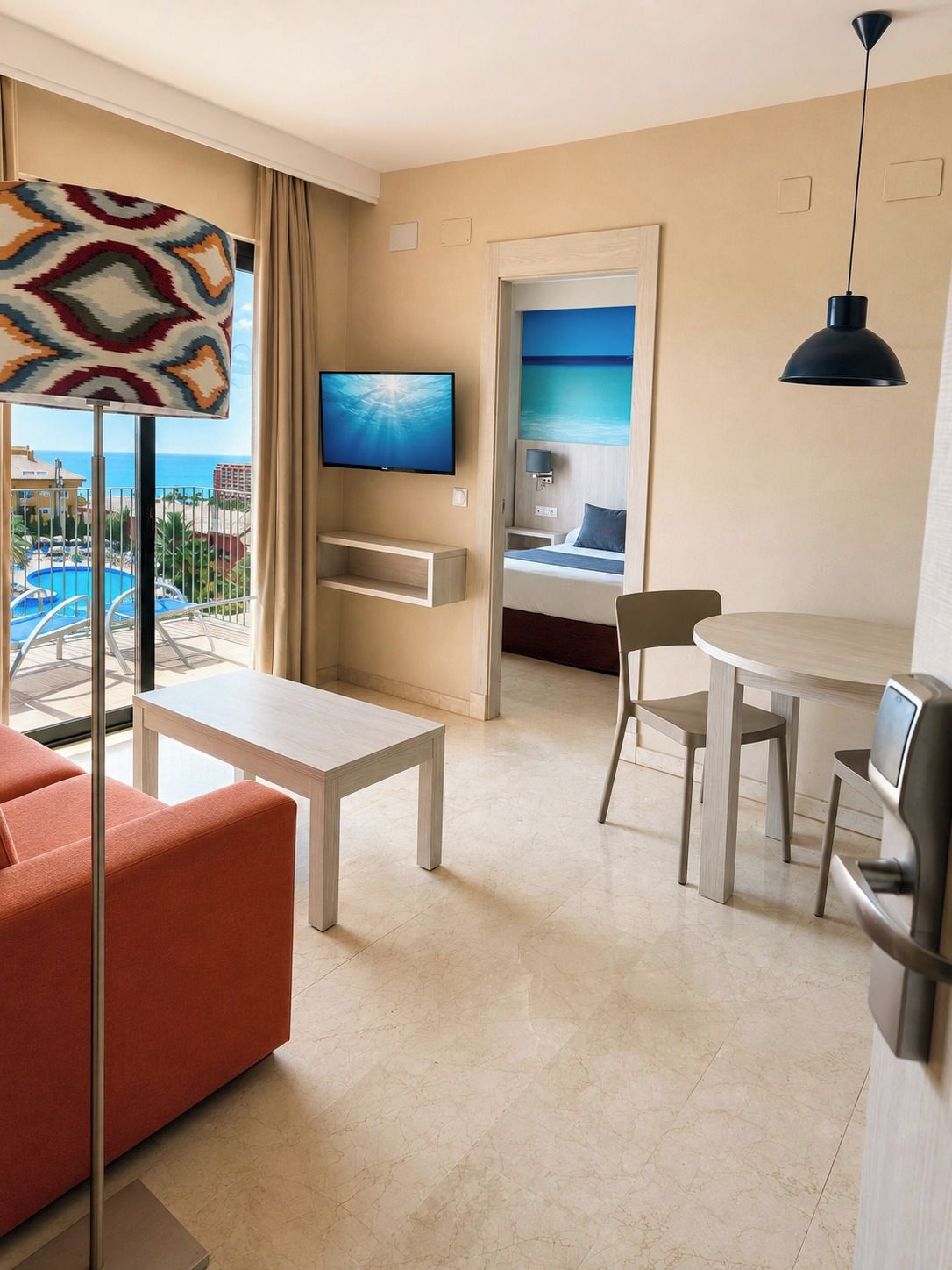 A hotel room with a balcony, a television, a dining area, and a bed.