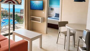 A hotel room with a balcony, a television, a dining area, and a bed.