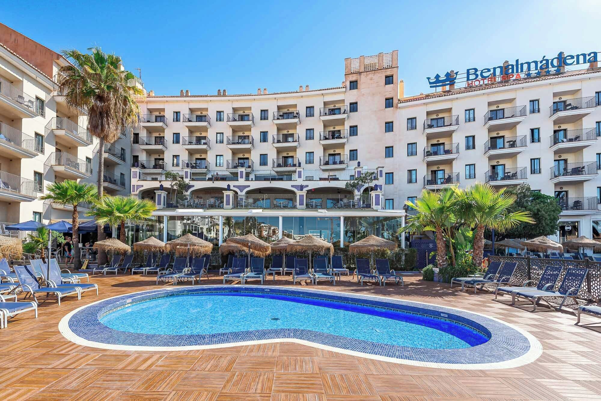 A hotel with a swimming pool, lounge chairs, and palm trees.