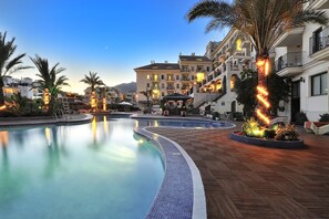 A pool area with a curved edge, palm trees, and a building with balconies in the background. - Benalmádena Palace - Hotel SPA & Apartments (Benalmádena)
