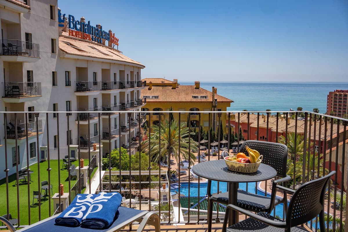 Un balcon d’hôtel avec une piscine, des chaises longues et une table où sont disposés des fruits.