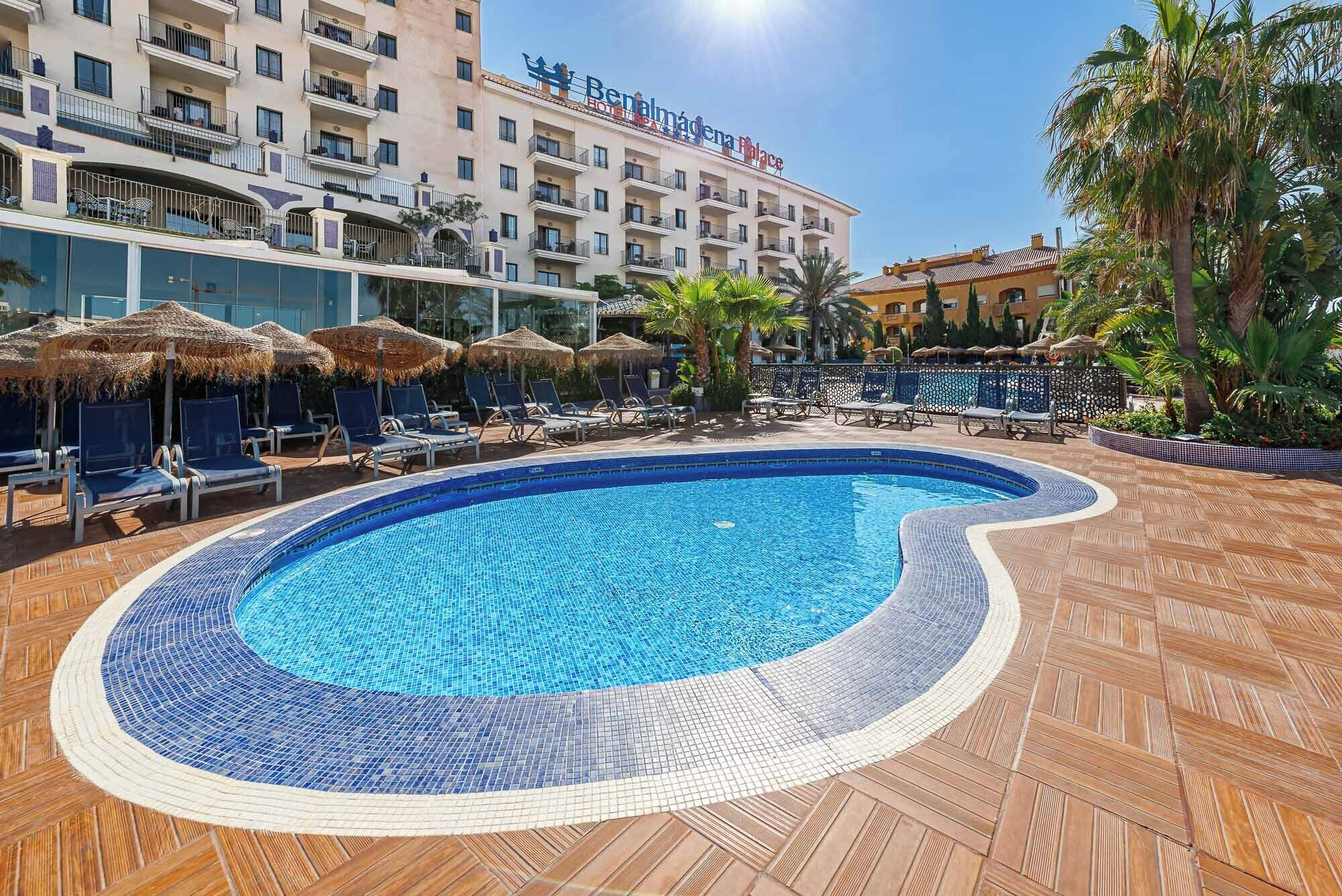 A hotel with a swimming pool surrounded by lounge chairs and umbrellas.