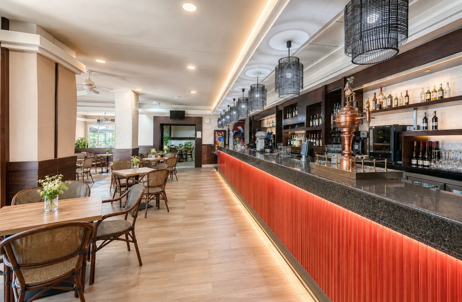 A bar area with a long counter, seating area with tables and chairs, and a variety of bottles and glasses on shelves.